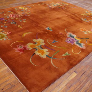 Rust area rug featuring large stylized multicolored floral patterns sits on rustic wood plank flooring.