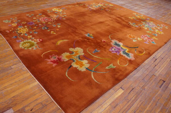 Rust area rug featuring large stylized multicolored floral patterns sits on rustic wood plank flooring.