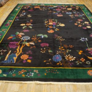 Ornate black rug with colorful floral motifs and a wide green border on light wood floors.