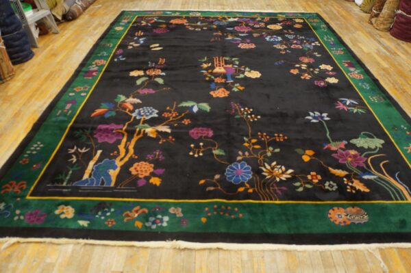 Ornate black rug with colorful floral motifs and a wide green border on light wood floors.