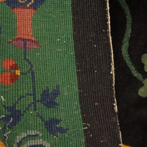 Close-up showing a green flatweave border with floral designs meeting a black cut pile field.