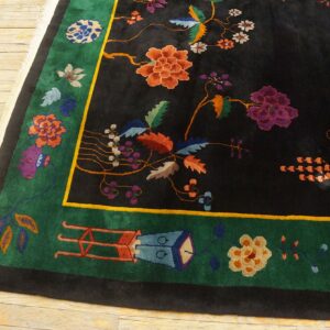 Black rug with vibrant orange and purple floral designs, bordered in green and outlined in yellow, on light wood flooring.