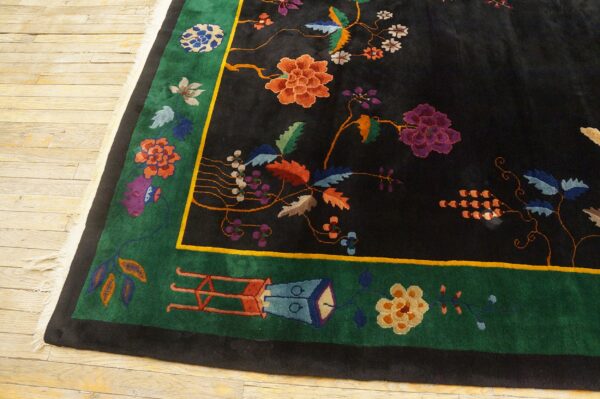Black rug with vibrant orange and purple floral designs, bordered in green and outlined in yellow, on light wood flooring.