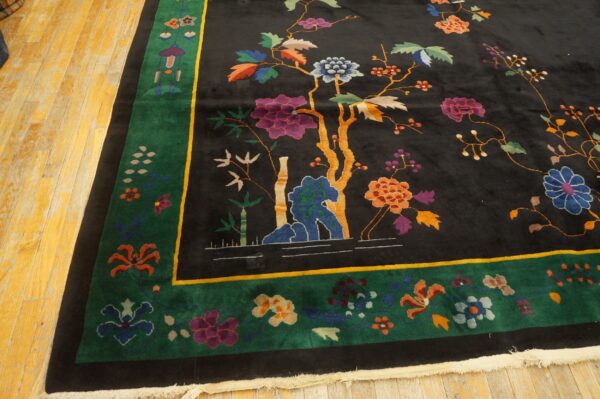 Black rug with colorful flowers and trees, bordered in green and gold, on light wood flooring.