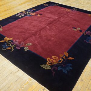 Plush red rug centered within a navy blue border featuring multicolored flowers and foliage on wood planks.