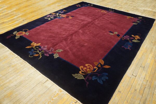 Plush red rug centered within a navy blue border featuring multicolored flowers and foliage on wood planks.