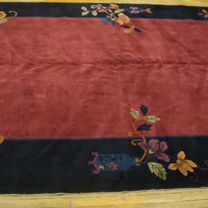 Deep red rug with a dark border featuring colorful floral motifs on light plank wood flooring.