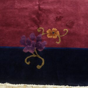 Plush burgundy and navy rug featuring purple and gold floral designs near visible cream fringe.