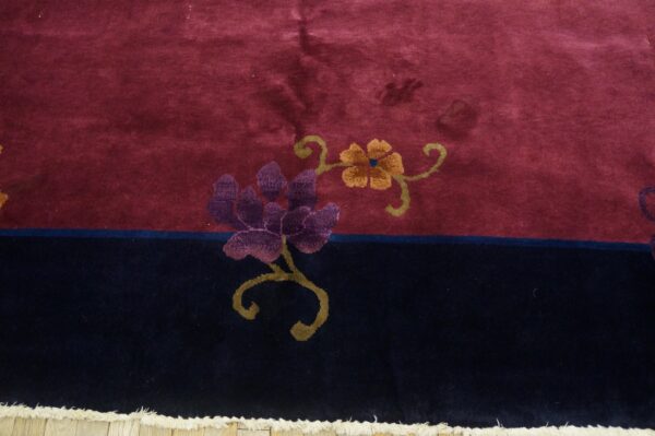 Plush burgundy and navy rug featuring purple and gold floral designs near visible cream fringe.
