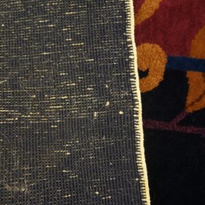 The rug's dark, woven backing contrasts with its dense, colorful pile featuring rust leaves on maroon and navy.
