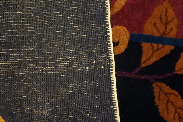The rug's dark, woven backing contrasts with its dense, colorful pile featuring rust leaves on maroon and navy.