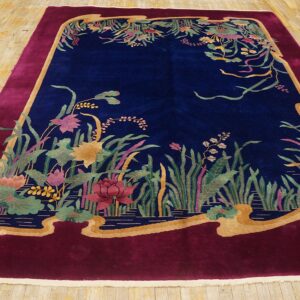 Plush navy rug featuring a water garden design surrounded by a wide scalloped burgundy border on wood flooring.