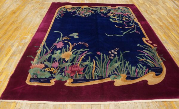 Plush navy rug featuring a water garden design surrounded by a wide scalloped burgundy border on wood flooring.