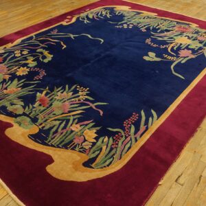 Navy blue rug with multicolored botanical borders, framed by gold and burgundy on light wood flooring.