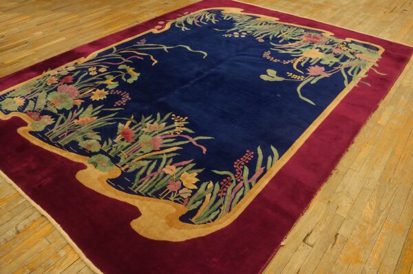 Navy blue rug with multicolored botanical borders, framed by gold and burgundy on light wood flooring.