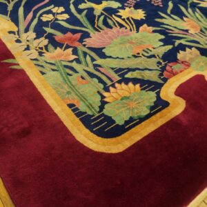 Plush rug with a navy floral field bordered by a curved gold line and solid crimson on wood flooring.