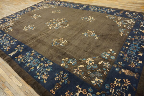 A brown rug with a deep indigo border displays scattered light blue and cream floral patterns.