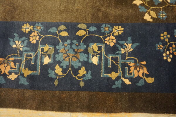 Close-up of a navy rug border featuring teal, gold, and olive floral motifs next to a brown field.