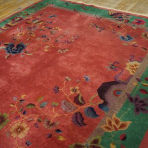 Plush red rug with multicolored floral designs and wide green borders on light wood flooring.