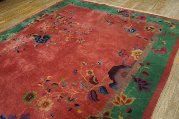 Plush red rug with multicolored floral designs and wide green borders on light wood flooring.