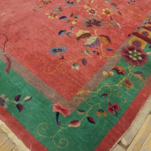 Close-up of a floral rug featuring a pink field, a green border, and fringe on wood floors.