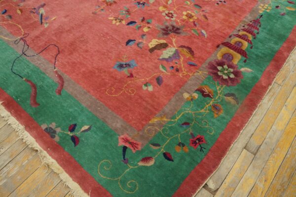Close-up of a floral rug featuring a pink field, a green border, and fringe on wood floors.