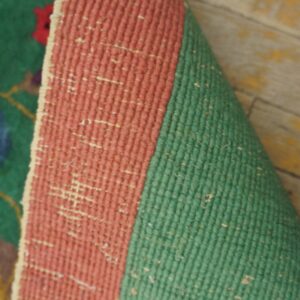 Rolled coral and green flatweave rug backing lies on worn wooden floorboards.