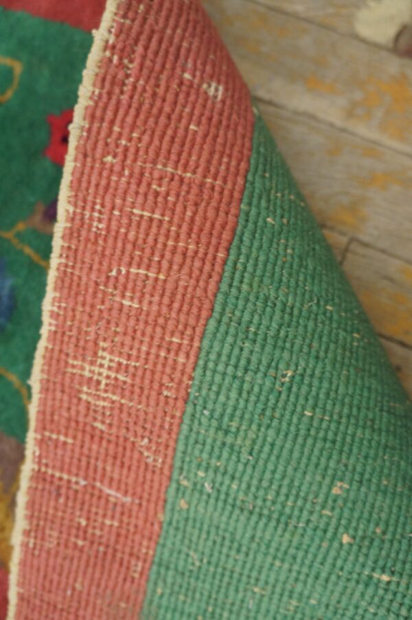 Rolled coral and green flatweave rug backing lies on worn wooden floorboards.