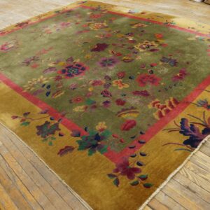 Olive green rug features multicolored flowers, a pink stripe, and a wide gold border on a wooden floor.