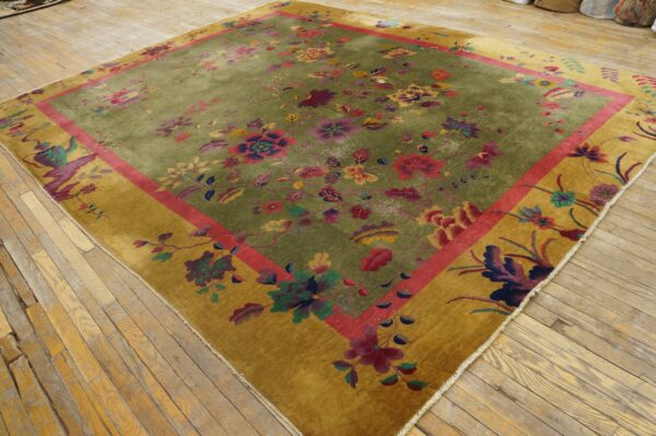 Olive green rug features multicolored flowers, a pink stripe, and a wide gold border on a wooden floor.