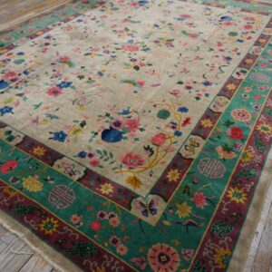 Beige rug with multicolored floral design and wide teal borders rests on rustic light gray wooden flooring.
