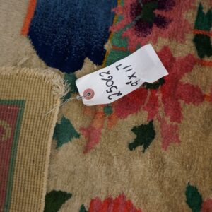 Close-up of a tan rug with bold red, blue, and green floral patterns and a visible product tag.