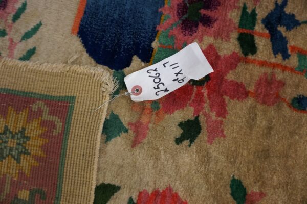Close-up of a tan rug with bold red, blue, and green floral patterns and a visible product tag.
