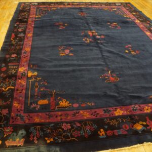 High-pile navy rug displaying detailed magenta and gold floral and object motifs on a bright wood floor.