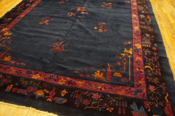 Dark blue high-pile rug featuring a scattered floral pattern and a multi-banded red and black border on wood floors.