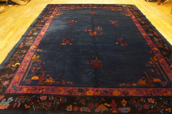 Deep indigo rug with scattered floral and vessel motifs, framed by intricate black and mauve borders.