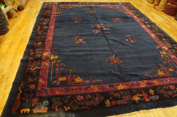 Deep navy blue area rug with detailed multi-color borders and scattered floral patterns lies on a light wood floor.
