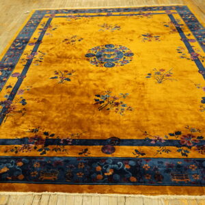 Plush golden yellow rug with blue floral medallion patterns, framed by a thick navy border on wood floor.