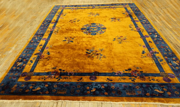 Plush golden yellow rug with blue floral medallion patterns, framed by a thick navy border on wood floor.