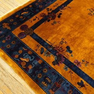 Gold high-pile rug with navy border and traditional floral designs resting on distressed wood planks.