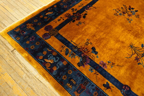 Gold high-pile rug with navy border and traditional floral designs resting on distressed wood planks.