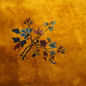 Plush gold rug featuring a delicate spray of blue, purple, and green botanical designs on a deep pile.