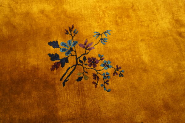 Plush gold rug featuring a delicate spray of blue, purple, and green botanical designs on a deep pile.