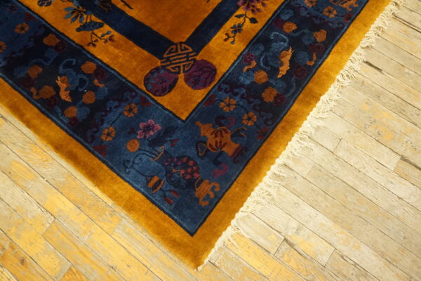 Plush gold rug with a navy, floral-patterned border and fringe rests on weathered wood planks.