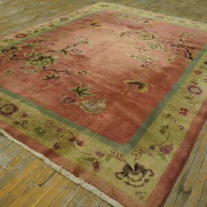 Rose and sage floral rug with olive border placed on distressed wooden floorboards.
