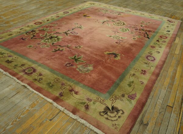 Rose and sage floral rug with olive border placed on distressed wooden floorboards.