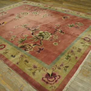 Low-pile rug with a detailed pink field and contrasting olive green floral border on rustic wood floors.