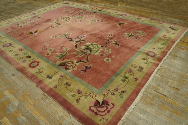 Low-pile rug with a detailed pink field and contrasting olive green floral border on rustic wood floors.