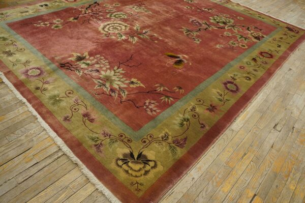 Low-pile dusty rose rug featuring sprawling botanical motifs and an olive border on light wood flooring.