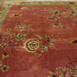 Rose and green floral rug with a thick border lies on distressed wooden floors.